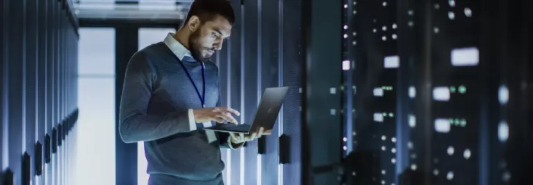 Persona controlla i dati su un laptop in una stanza server.