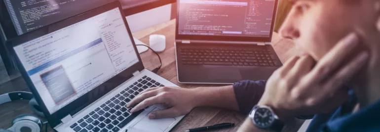 Persona al lavoro su più laptop con codice sullo schermo.