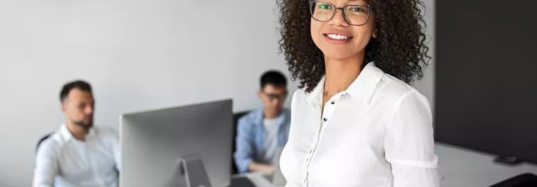 Persona sorridente con occhiali in un ufficio davanti a computer.