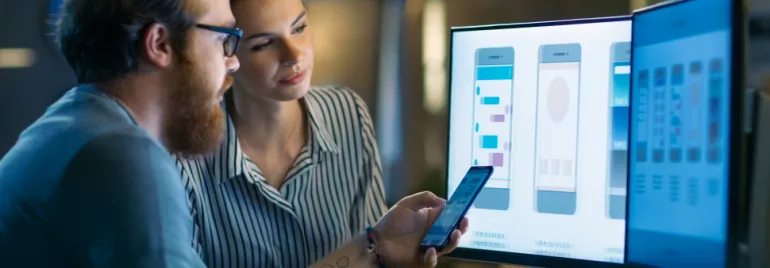 Due persone analizzano interfacce app su schermo e telefono.