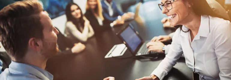 Riunione in ufficio con persone che sorridono attorno a un tavolo.
