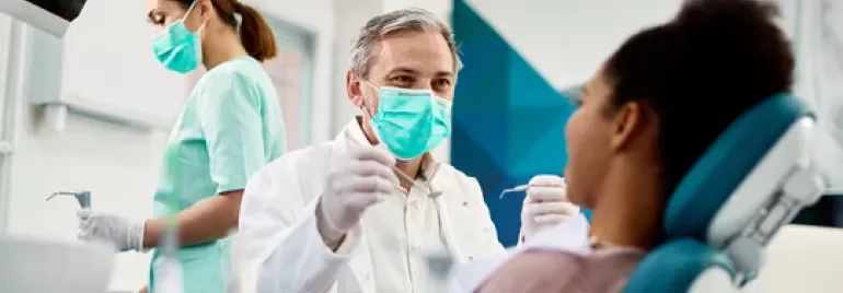 Dentista con maschera e paziente in studio odontoiatrico.