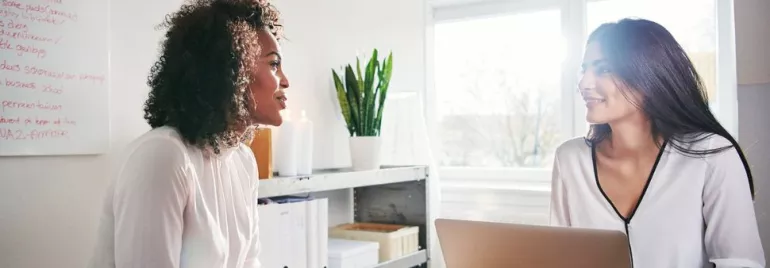 Due persone conversano in un ufficio luminoso con un laptop aperto sul tavolo.