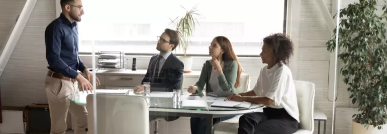 Persona in piedi di fronte a tre persone sedute in una sala riunioni.