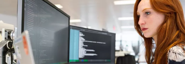 Persona che lavora al computer con codice su due monitor.