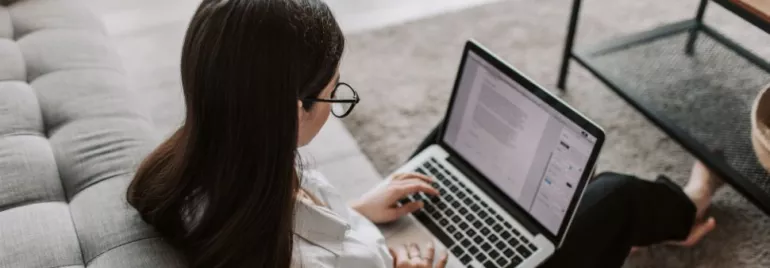 Persona con occhiali lavora al computer portatile su un divano.