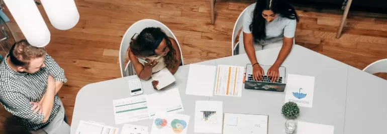 Persone al lavoro in un ufficio con documenti e laptop su un tavolo.