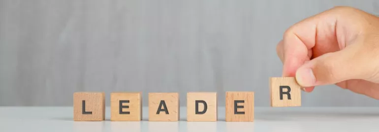 Blocchi di legno con la parola “LEADER” su sfondo grigio.