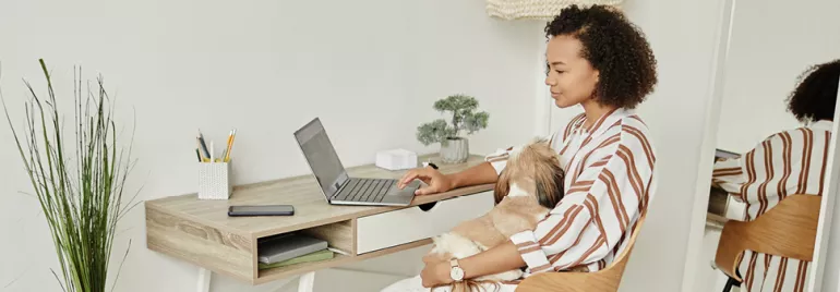 Persona al computer con un cane in braccio.