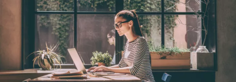 Persona al computer vicino a una finestra con piante.
