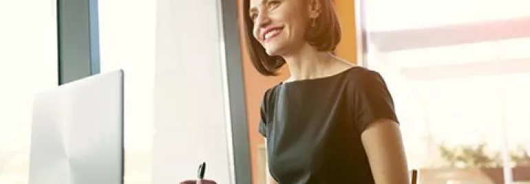 Persona sorridente seduta al tavolo con laptop aperto.