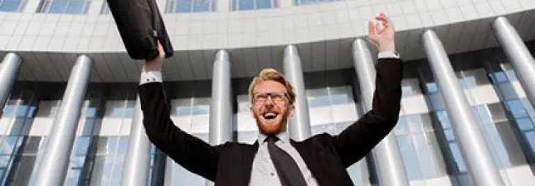 Persona sorridente solleva una valigetta davanti a un edificio moderno.