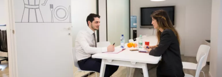 Due persone in riunione sedute a un tavolo bianco in ufficio moderno.