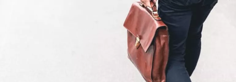 Persona che cammina con una borsa di pelle marrone.