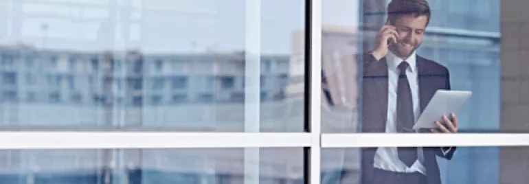 Persona che parla al telefono e guarda un tablet, vista attraverso una finestra.