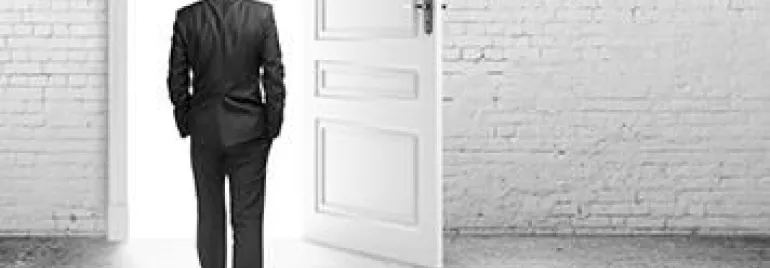 Persona in abito si allontana verso una porta aperta, luce intensa all'esterno.