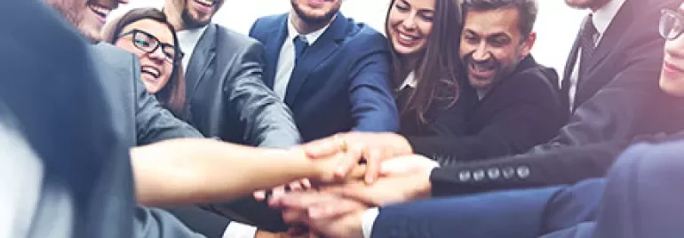Gruppo di persone in abiti formali che si danno la mano in cerchio.