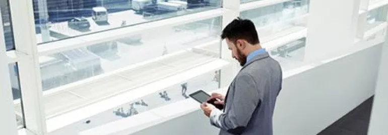 Persona in abito grigio guarda un tablet vicino alla finestra.