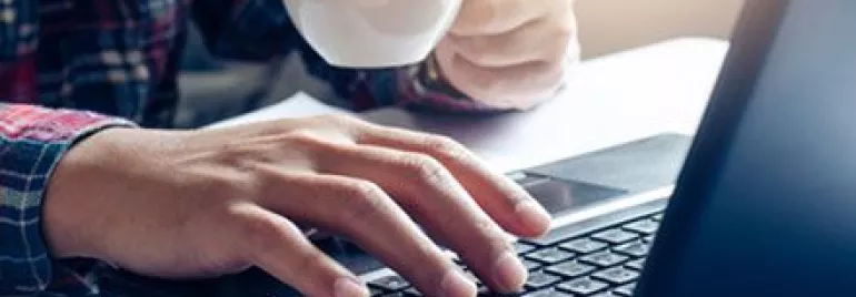 Persona al lavoro su un laptop tenendo una tazza da caffè.