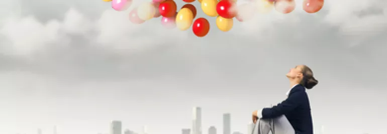 Persona seduta su un tetto osserva palloncini colorati nel cielo grigio.