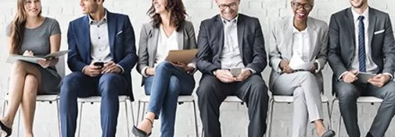 Gruppo di persone sedute in attesa, indossano abiti formali.