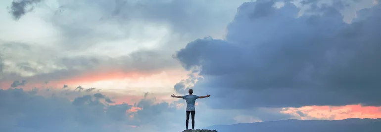 Persona su una roccia con le braccia aperte verso il cielo al tramonto.