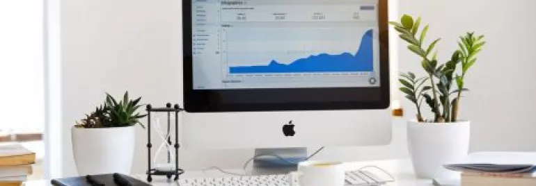 Scrivania con computer e grafico a schermo, piante e tazza di caffè.
