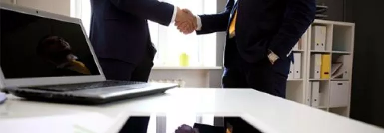 Stretta di mano in ufficio con dispositivi sul tavolo.