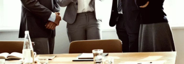 Persone in abiti formali discutono davanti a un tavolo da riunione.