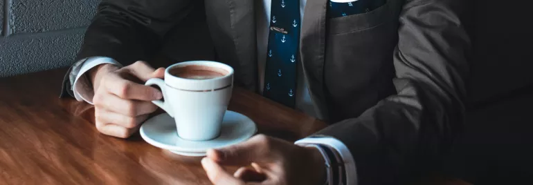 Persona in abito tiene una tazza di caffè su tavolo di legno.