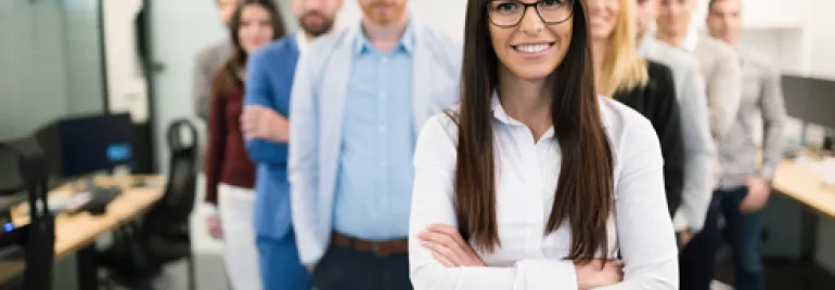 Gruppo di persone in ufficio, persona in primo piano con occhiali sorridente.