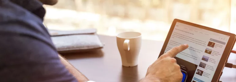 Persona che usa un tablet al tavolo con tazza di caffè.