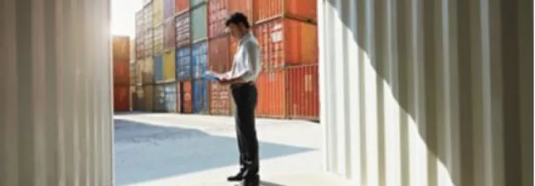 Persona in piedi vicino a container colorati, con documenti in mano.