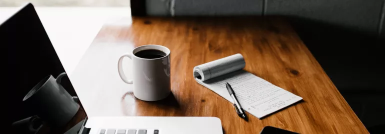 Scrivania con laptop, tazza di caffè e blocco note.