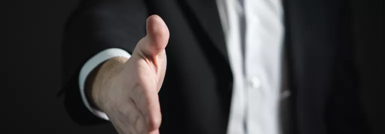 Persona in abito formale tende la mano per una stretta.