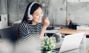 Persona con cuffie davanti a un laptop, sorridente.