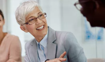 Persona sorridente in un meeting, indossa occhiali e abito formale.