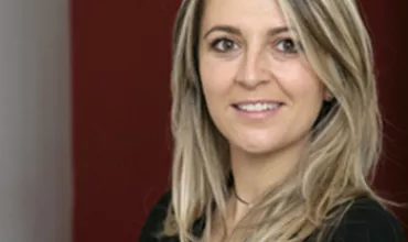 Persona sorridente con capelli biondi e lunghi, sfondo rosso.