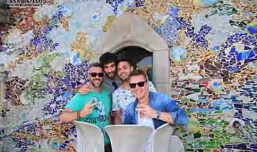 Quattro persone sorridenti davanti a un colorato mosaico a Barcellona.